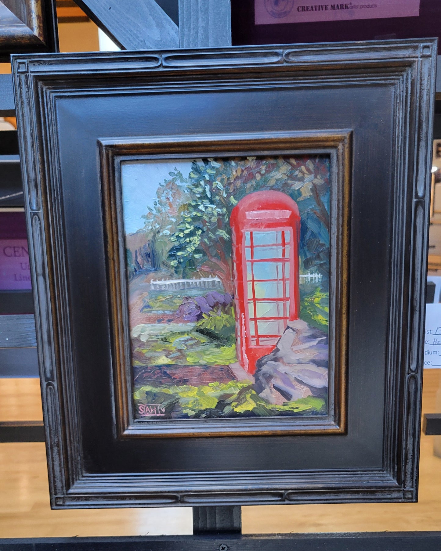Framed artwork of a red telephone box in a garden setting