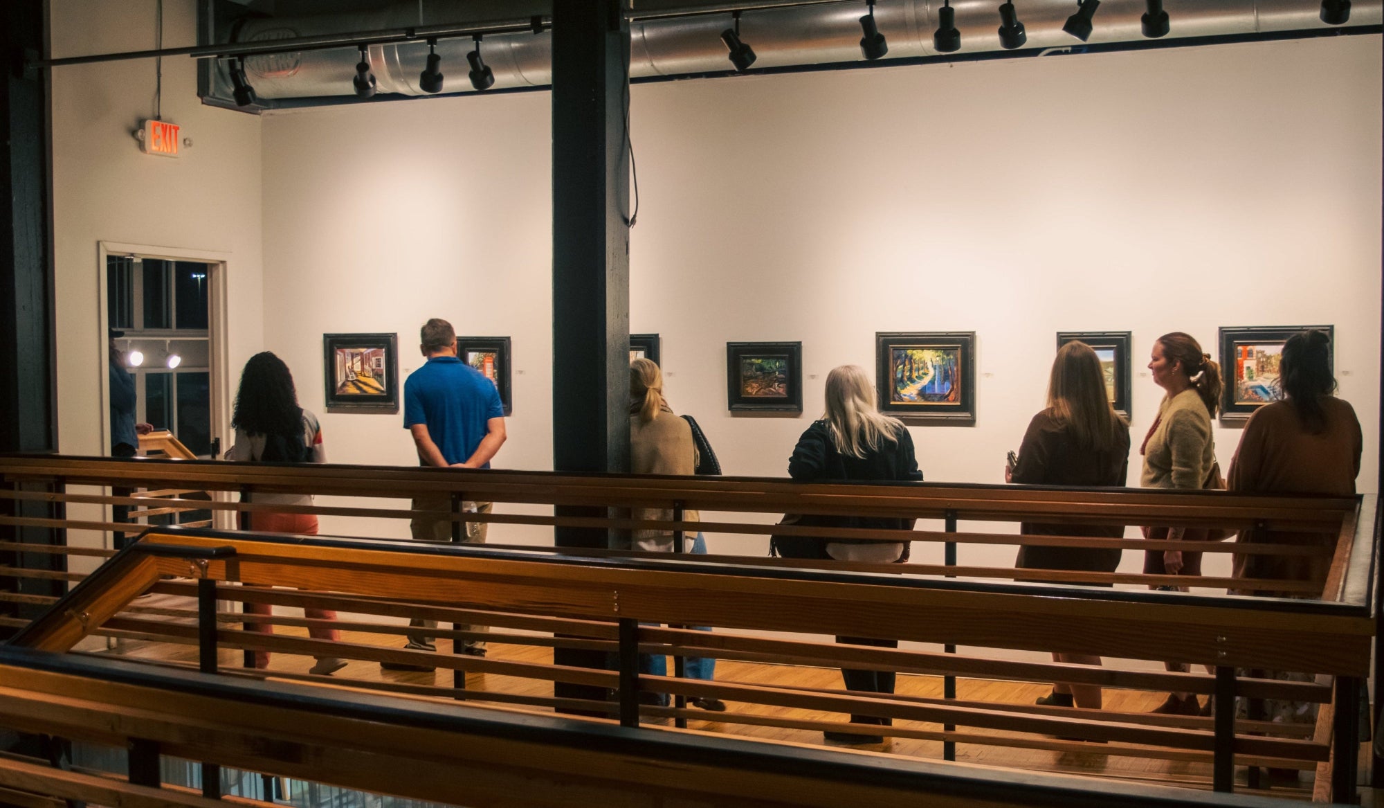People observing art pieces on a wall in an exhibition setting.